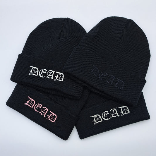 BLACK knitted acrylic beanie hat featuring an embroidered cuff that reads DEAD in a medieval gothic font. Embroidery colours shown, white, black, pink and silver.