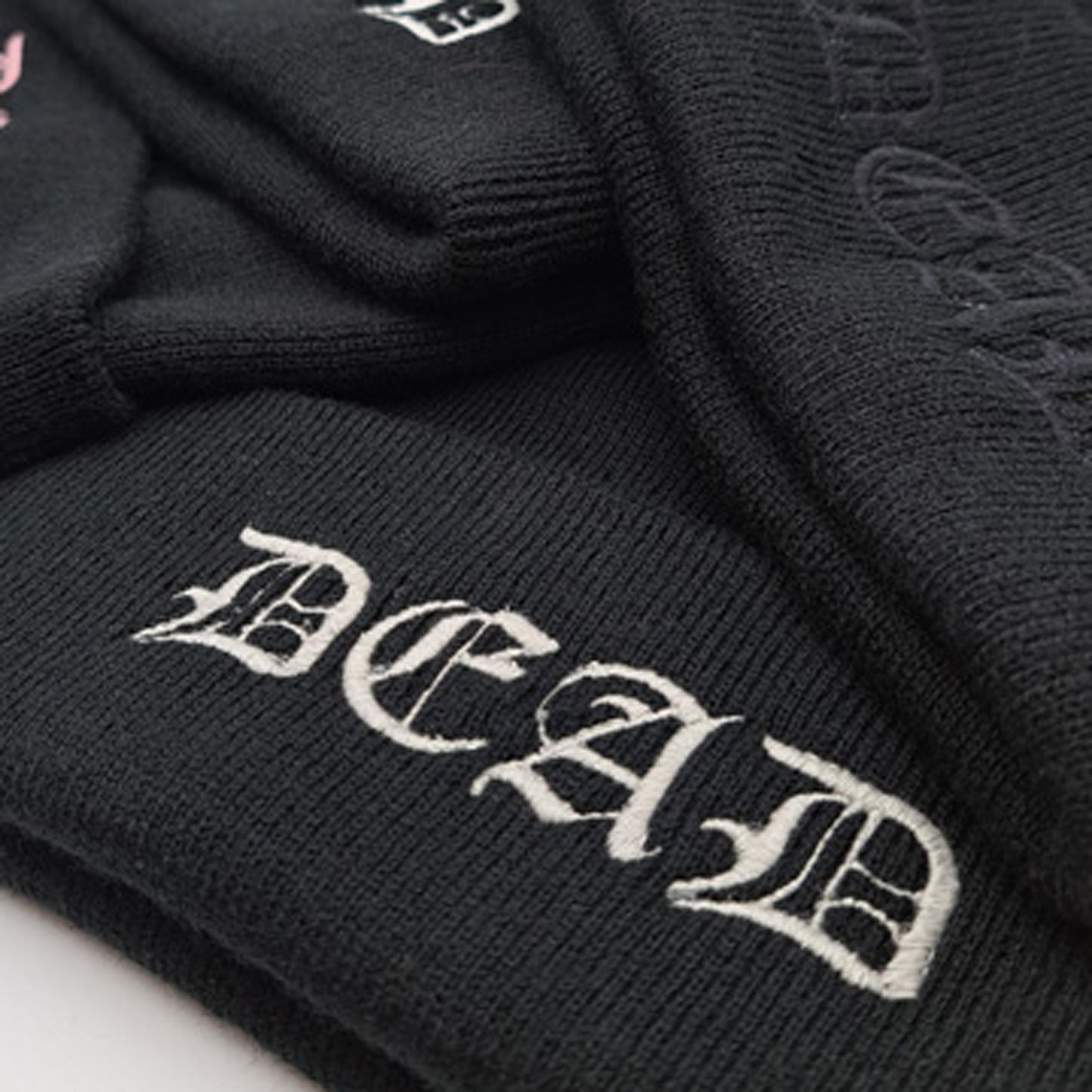 Close up of BLACK knitted beanie hat featuring an embroidered cuff that reads DEAD in a medieval gothic font in silver colourway.