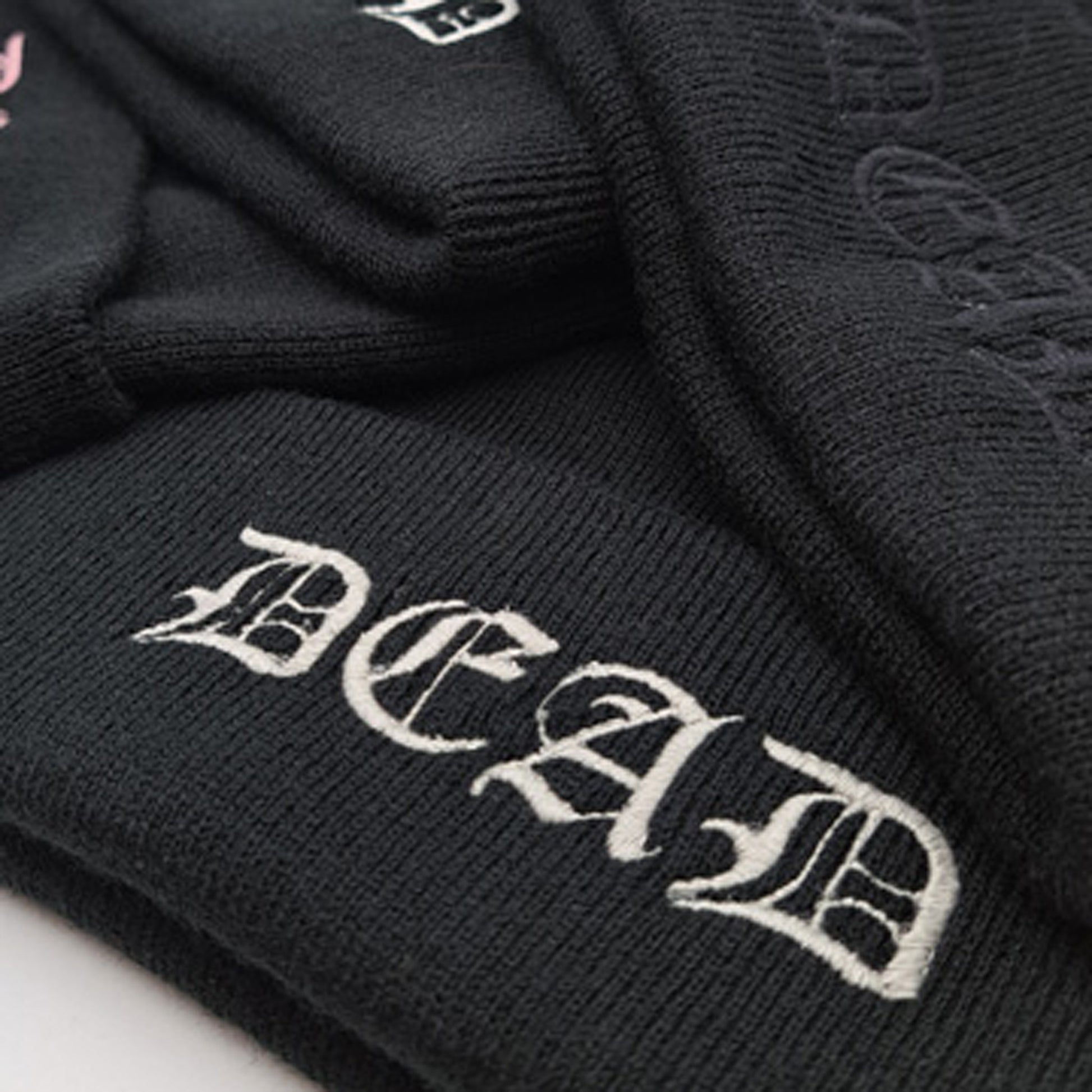 Close up of BLACK knitted beanie hat featuring an embroidered cuff that reads DEAD in a medieval gothic font in silver colourway.