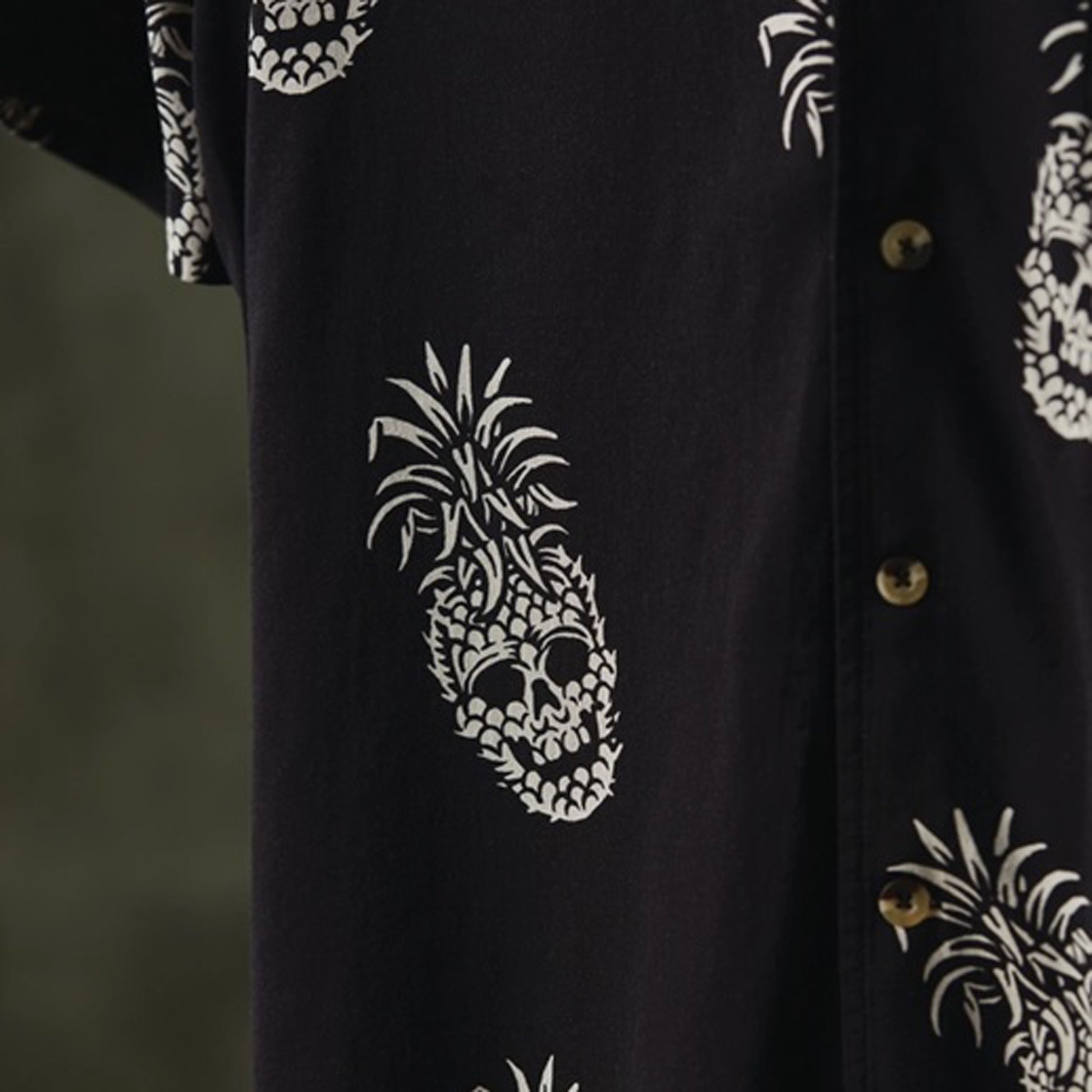 Close-up of a black button-up shirt featuring a white pineapple skull print and tortoise shell-like buttons.