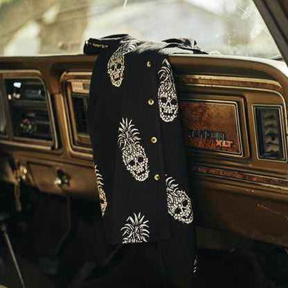 A black button-up shirt with white skull and pineapple prints draped over the dashboard of a vintage car interior.